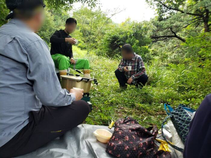 People sitting around a tarp in the grass drinking coffee