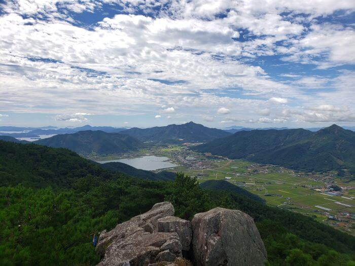 A large rock jutting out into a nice view of mountains, water, rice fields, and villages