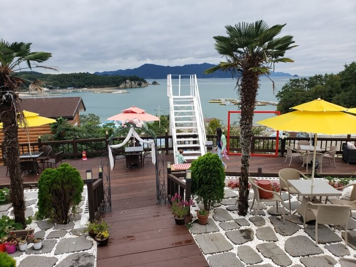 Outdoor patio full of decorations and seats including umbrellas and palm trees with a beautiful sea view