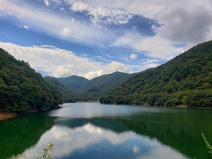 A calm reservoir surrounded by mountains reflecting blue sky and clouds