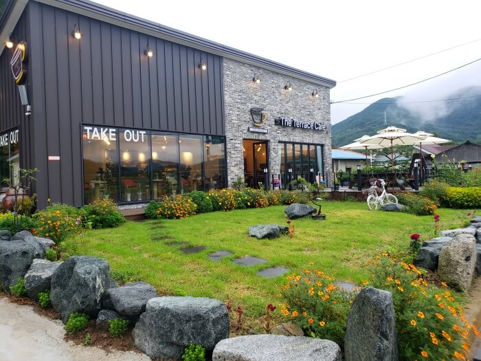 A view of the outside of the The Terrace Café building with a grassy yard and flowers