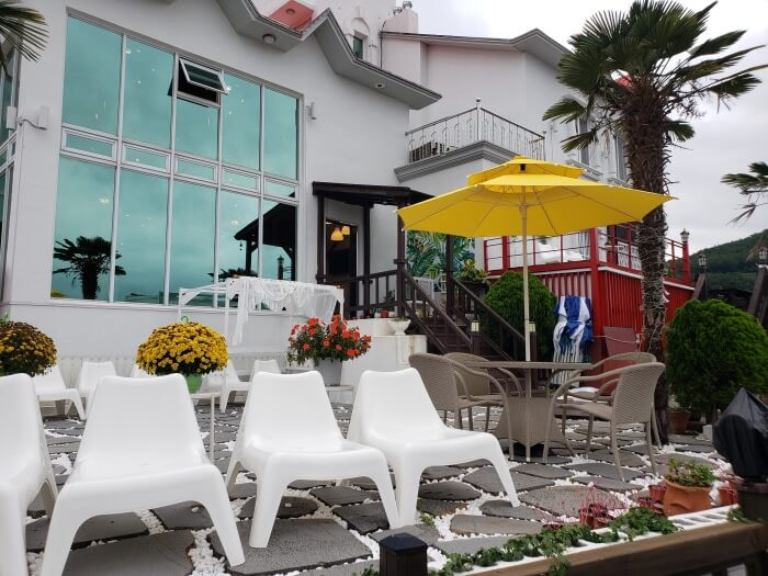 White chairs in an outdoor patio area next to windows and umbrellas and palm trees