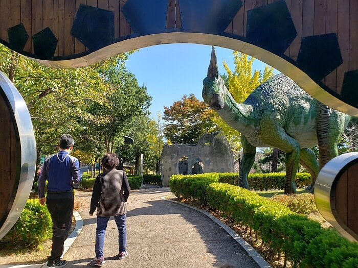 Couple walking past dinosaur structures and bushes outside