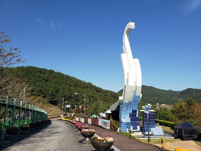 A dinosaur-shaped structure along a road with potted flowers and mountains in the background