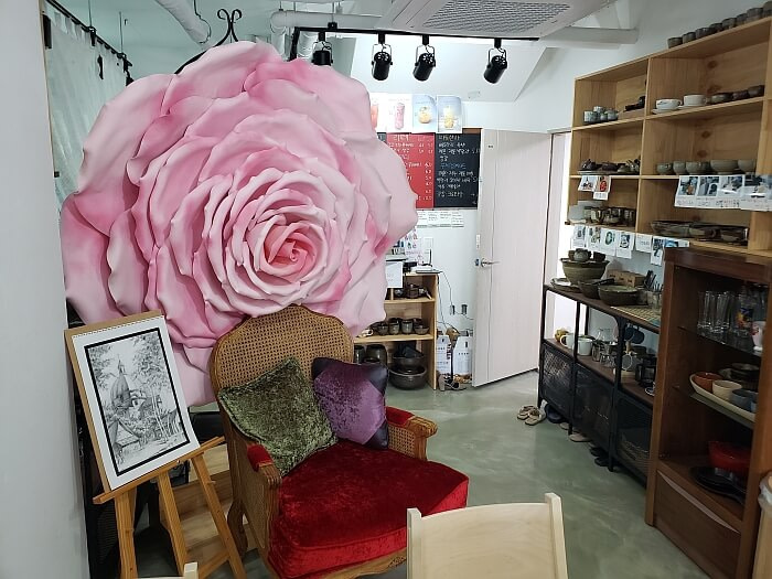 A large, pink, handmade flower against a red chair across from shelves with pottery and dish decorations