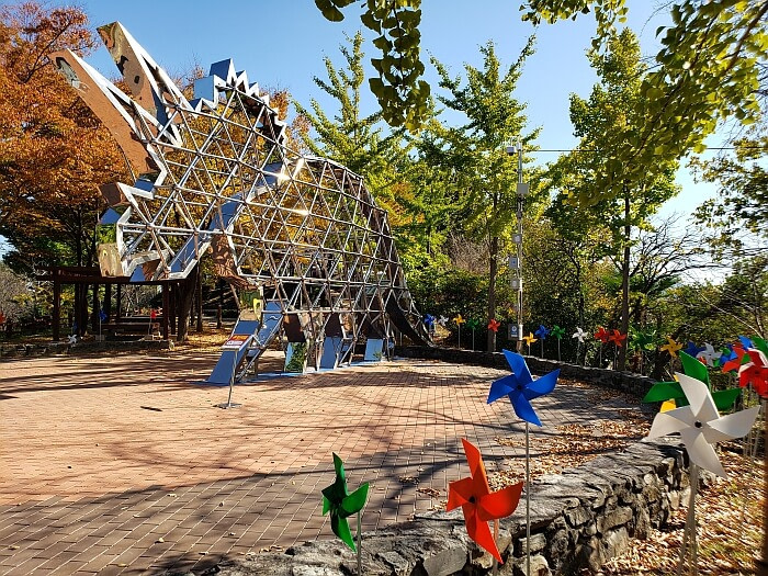 Steel bars making up a dinosaur shape surrounded by pinwheels in a playground