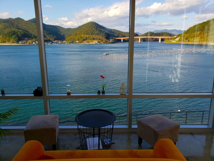 A sofa at An Café overlooking a coastal view with a bridge and mountains in Goseong, Gyeongnam, Korea