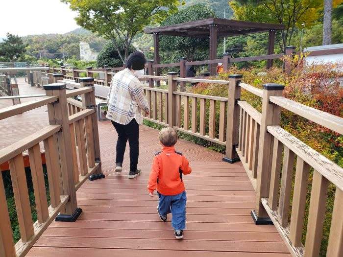 A woman inviting a toddler to walk with her on a wooden boardwalk