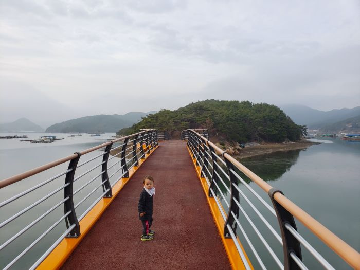 A toddler looking over his shoulder while crossing a bridge to an island.