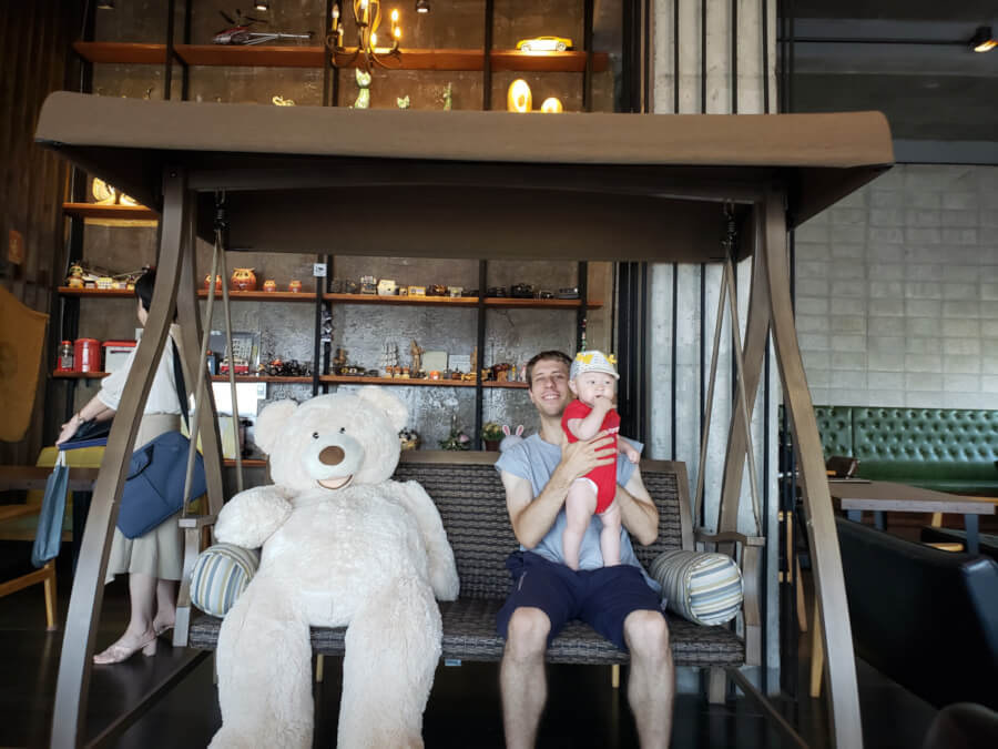 Nate holding Noah on swing with big white teddy bear