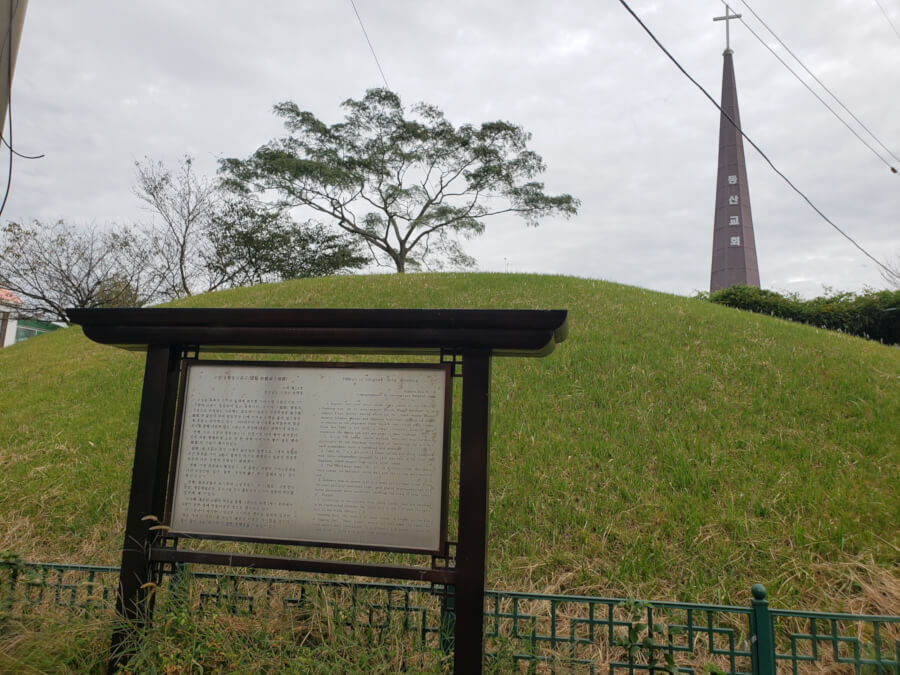 Smaller tomb with a signpost in front and a church behind it