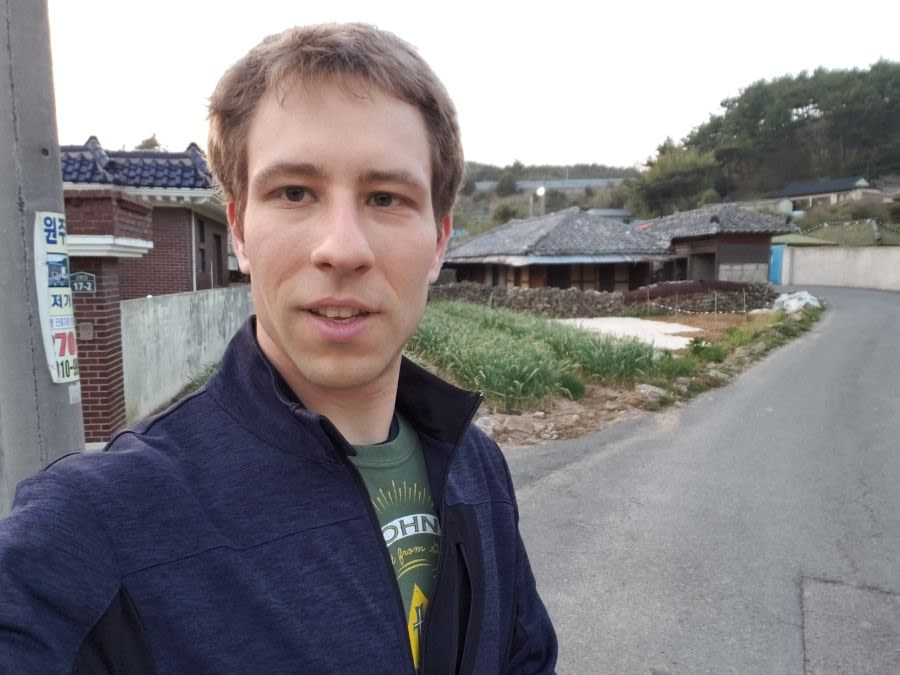 Nate next to garlic growing along a hanok and stone wall in a village in Goseong, Korea, 2018
