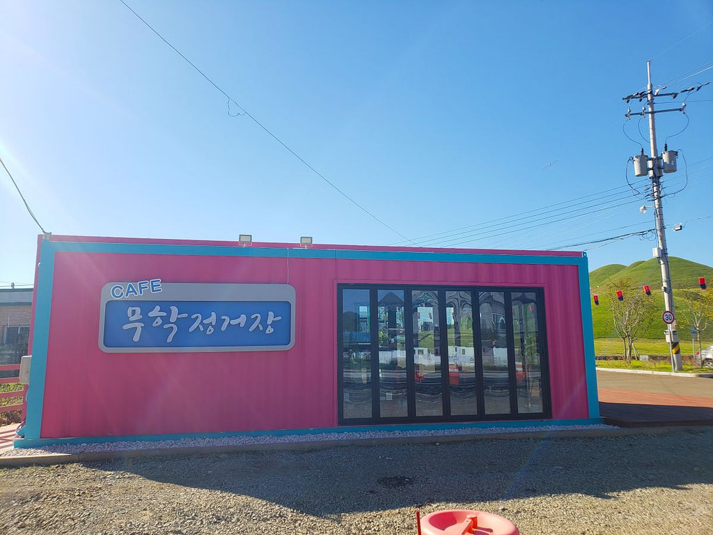 A pink container housing a café called Muhak Station next to ancient burial mounds